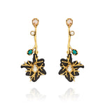 Brinco longo preto e dourado Camila Klein Peregrinar, com design floral escultural, metais com banho em ouro velho, resina preta e cristais em tons champagne, branco e verde-turquesa. O modelo possui haste alongada e composição assimétrica de elementos, com cristal central em destaque na flor. Uma peça sofisticada e marcante, ideal para valorizar produções contemporâneas e elegantes.