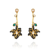 Brinco longo preto e dourado Camila Klein Peregrinar, com design floral escultural, metais com banho em ouro velho, resina preta e cristais em tons champagne, branco e verde-turquesa. O modelo possui haste alongada e composição assimétrica de elementos, com cristal central em destaque na flor. Uma peça sofisticada e marcante, ideal para valorizar produções contemporâneas e elegantes.