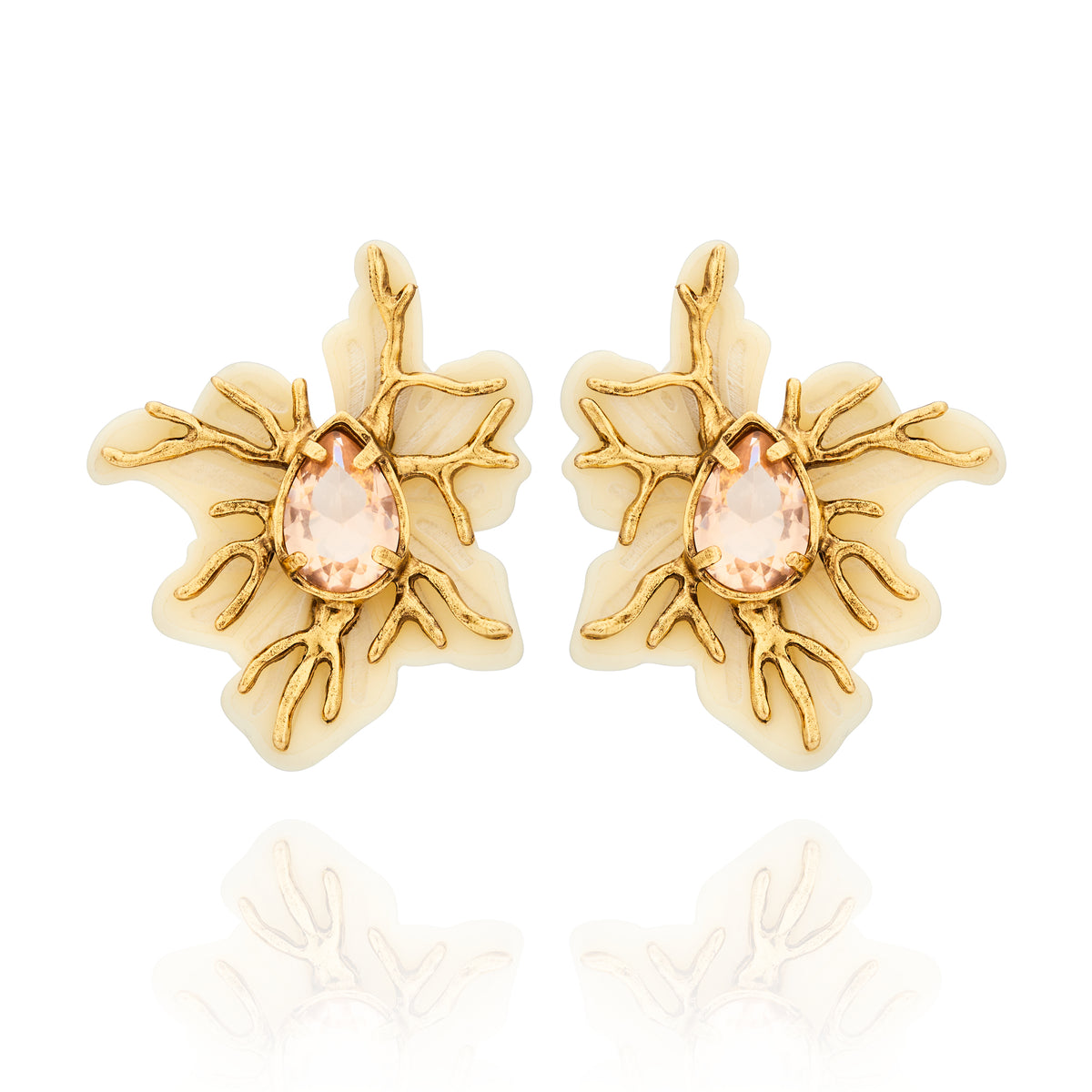 Brinco Médio Marfim Ouro Peregrinar Camila Klein, com design floral orgânico inspirado em elementos da natureza, confeccionado em resina marfim com detalhes metálicos em ramificações e acabamento em banho de ouro velho. Possui cristal central em formato de gota, com tonalidade rosada suave e lapidação facetada que proporciona brilho delicado. A combinação entre o marfim, o dourado e o cristal cria uma peça sofisticada, marcante e elegante para complementar diferentes produções.