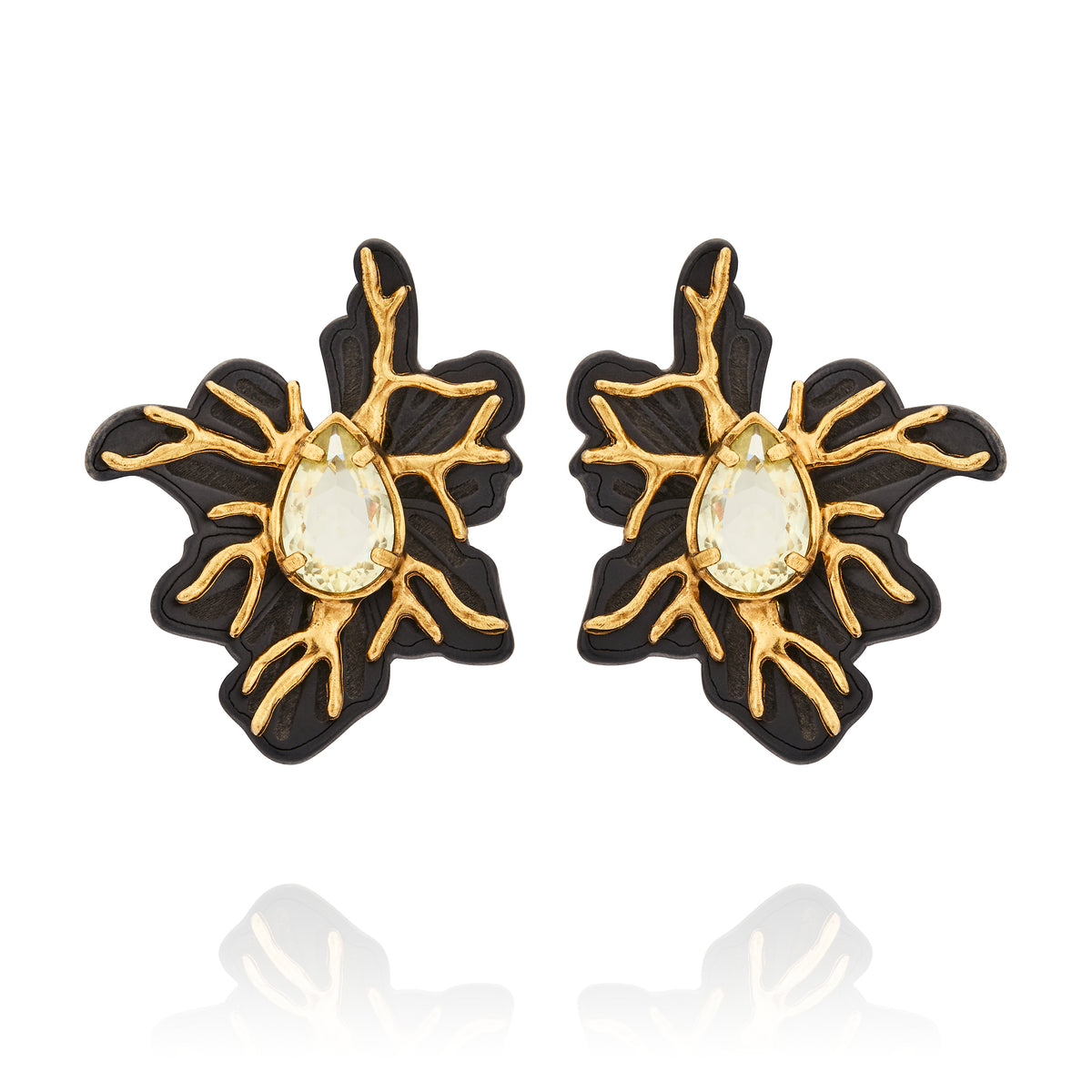 Brinco Médio Preto Ouro Peregrinar Camila Klein, com design floral orgânico e sofisticado, confeccionado em resina preta com detalhes metálicos de ramificações e acabamento em banho de ouro velho. Possui cristal central em formato de gota com tonalidade clara e acabamento facetado, criando contraste elegante entre o preto, o dourado e o brilho do cristal. A composição inspirada em elementos da natureza destaca o estilo marcante e contemporâneo da peça.