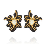 Brinco Médio Preto Ouro Peregrinar Camila Klein, com design floral orgânico e sofisticado, confeccionado em resina preta com detalhes metálicos de ramificações e acabamento em banho de ouro velho. Possui cristal central em formato de gota com tonalidade clara e acabamento facetado, criando contraste elegante entre o preto, o dourado e o brilho do cristal. A composição inspirada em elementos da natureza destaca o estilo marcante e contemporâneo da peça.