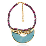 Colar Camila Klein com pedras naturais em tons de roxo, azul e dourado, destacando uma composição sofisticada e vibrante. O modelo apresenta contas esféricas coloridas, detalhes dourados e um elegante elemento central em formato semicircular azul. Uma peça autoral que combina frescor, personalidade e elegância para produções de verão.