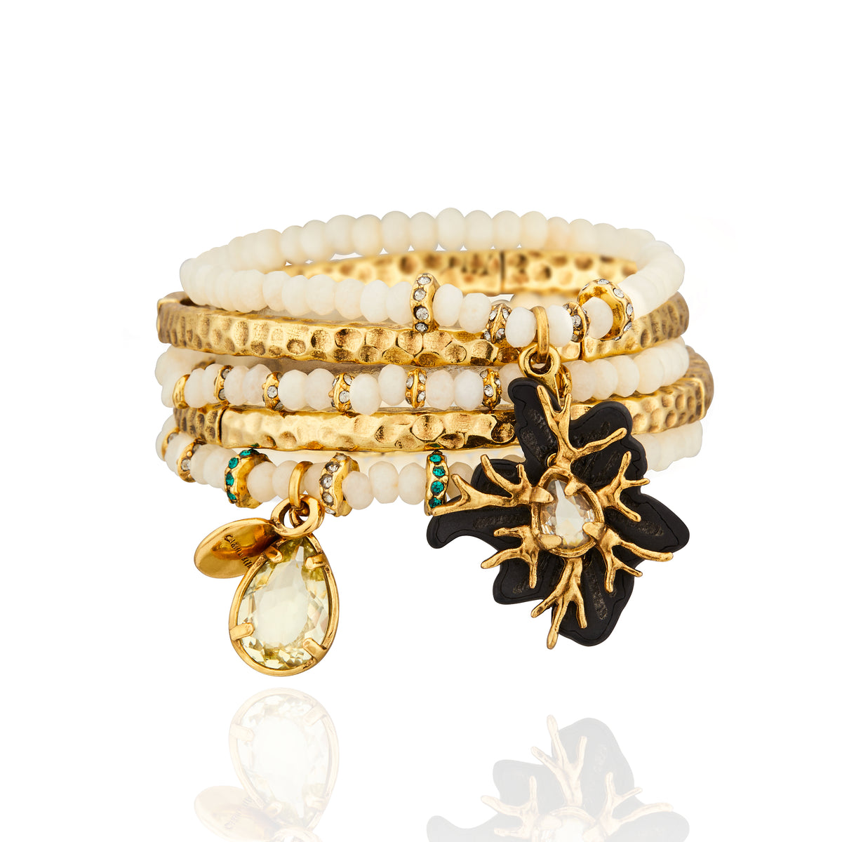 Kit Pulseira Marfim Preto Ouro Peregrinar da Camila Klein, composto por pulseiras de jade creme leitoso, cristais e metais com banho de ouro velho. O conjunto combina contas marfim, elementos dourados, cristais transparentes e verde-azulados. Destaque para a pulseira com flor estilizada em resina preta, estrutura dourada e cristal central, além de pingentes em formato de gota. Composição orgânica e sofisticada, fotografada sobre fundo branco com reflexo.
