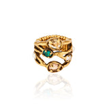 Meio Anel Cristais Ouro Peregrinar da Camila Klein, em metal com banho de ouro velho, com design orgânico e vazado formado por linhas irregulares. O anel apresenta cristais em diferentes tonalidades, incluindo cristal transparente, verde-azulado e rosado, aplicados em diferentes pontos da peça. O aro possui acabamento texturizado e detalhes que remetem a formas naturais, com uma composição sofisticada e artesanal. Fotografia do anel sobre fundo branco, com reflexo da peça na superfície.